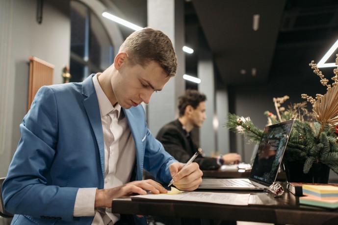 Focused businessman writing notes at desk with Christmas decorations and laptop in modern office.