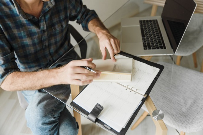 A person taking notes at a desk with a laptop and notebook, emphasizing productivity and planning.